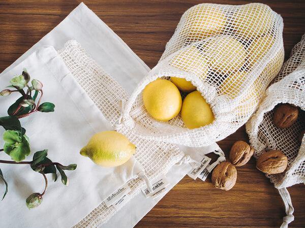 A variety of breathable mesh produce bags on a kitchen counter containing fresh fruits and vegetables like apples, oranges, carrots, and leafy greens. Each bag is tied with a drawstring, showcasing colorful produce through the mesh fabric. A variety of breathable mesh produce bags on a kitchen counter containing fresh fruits and vegetables like apples, oranges, carrots, and leafy greens. Each bag is tied with a drawstring, showcasing colorful produce through the mesh fabric.