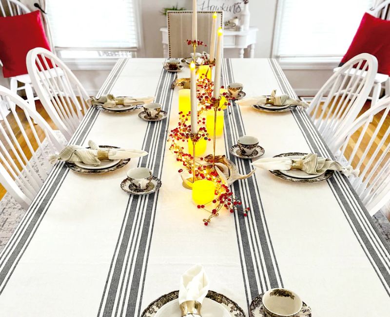 A dining table set with a striped tablecloth featuring a red border. The tablecloth has alternating stripes, with a solid red border around the edges. A dining table set with a striped tablecloth featuring a red border. The tablecloth has alternating stripes, with a solid red border around the edges.
