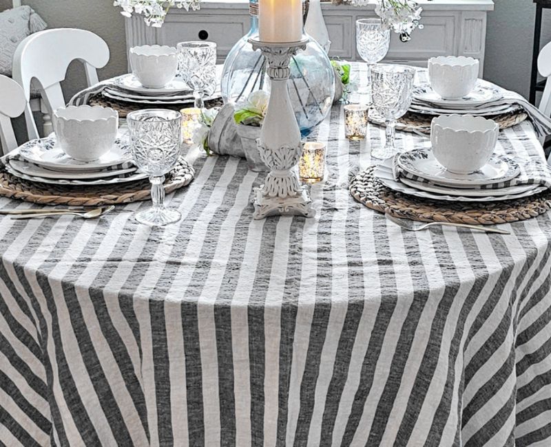 Cozy dining room with a table set for a meal, featuring a bold and colorful striped tablecloth with red, white, and blue stripes, plates, glasses, cutlery, natural light, and potted plants adding a touch of greenery Cozy dining room with a table set for a meal, featuring a bold and colorful striped tablecloth with red, white, and blue stripes, plates, glasses, cutlery, natural light, and potted plants adding a touch of greenery