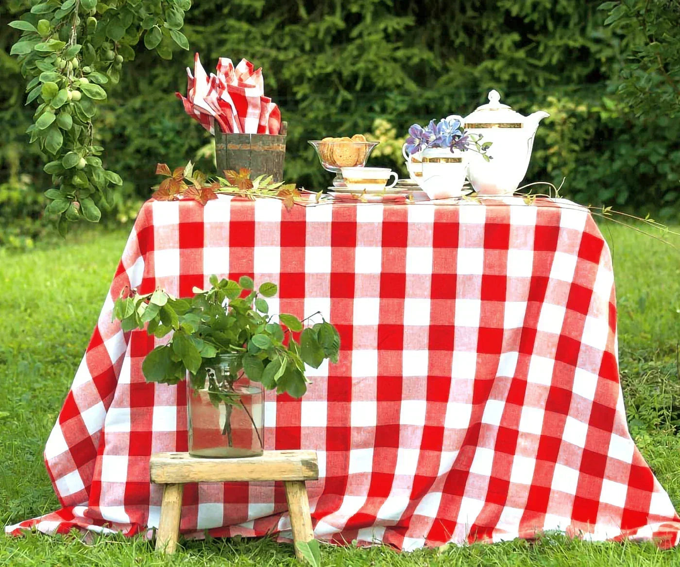 Outdoor picnic table covered with a classic red and white buffalo plaid tablecloth in a lush garden setting. Outdoor picnic table covered with a classic red and white buffalo plaid tablecloth in a lush garden setting.