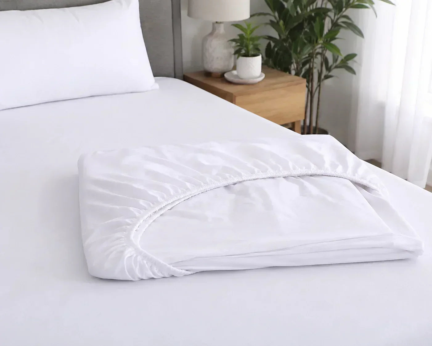Neatly folded white fitted sheet with elastic edges resting on a freshly made bed in a bright, modern bedroom. Neatly folded white fitted sheet with elastic edges resting on a freshly made bed in a bright, modern bedroom.