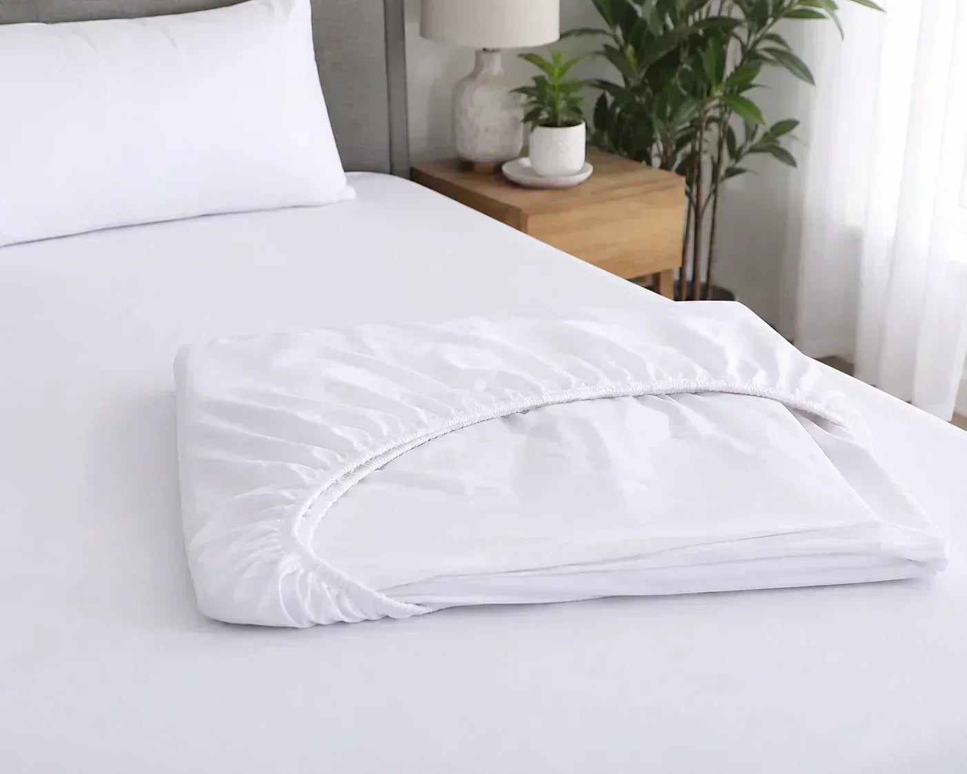 Neatly folded white fitted sheet with elastic edges resting on a freshly made bed in a bright, modern bedroom. Neatly folded white fitted sheet with elastic edges resting on a freshly made bed in a bright, modern bedroom.