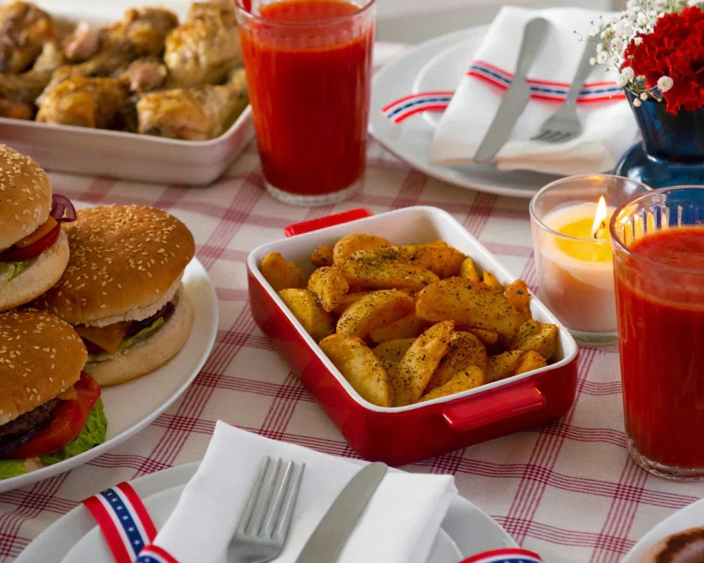 Memorial Day BBQ table setup with cheeseburgers, roasted potato wedges, grilled chicken, red drinks, candles, and patriotic napkins for a festive summer gathering. Memorial Day BBQ table setup with cheeseburgers, roasted potato wedges, grilled chicken, red drinks, candles, and patriotic napkins for a festive summer gathering.