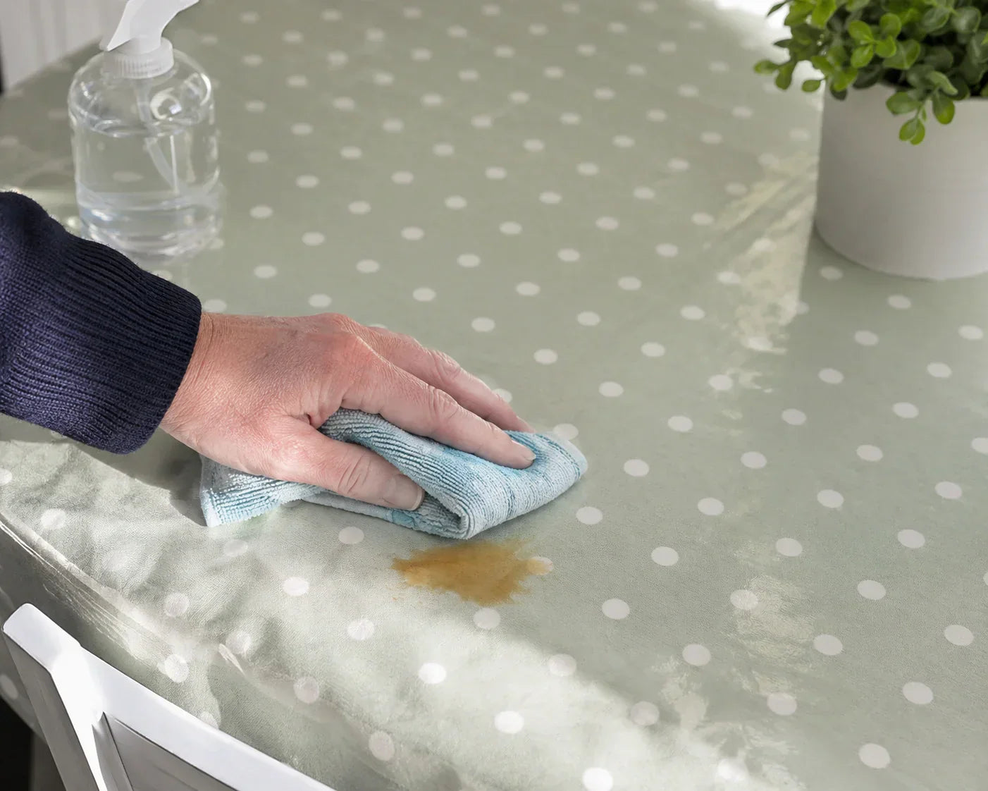 Person wiping a stain from a green polka dot oilcloth tablecloth with a microfiber cloth in a bright kitchen setting. Person wiping a stain from a green polka dot oilcloth tablecloth with a microfiber cloth in a bright kitchen setting.