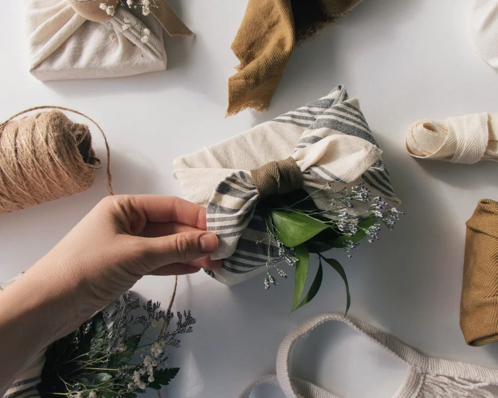 Hands tying a striped cloth napkin around a gift with greenery and natural fabric accents for sustainable gift wrapping. Hands tying a striped cloth napkin around a gift with greenery and natural fabric accents for sustainable gift wrapping.