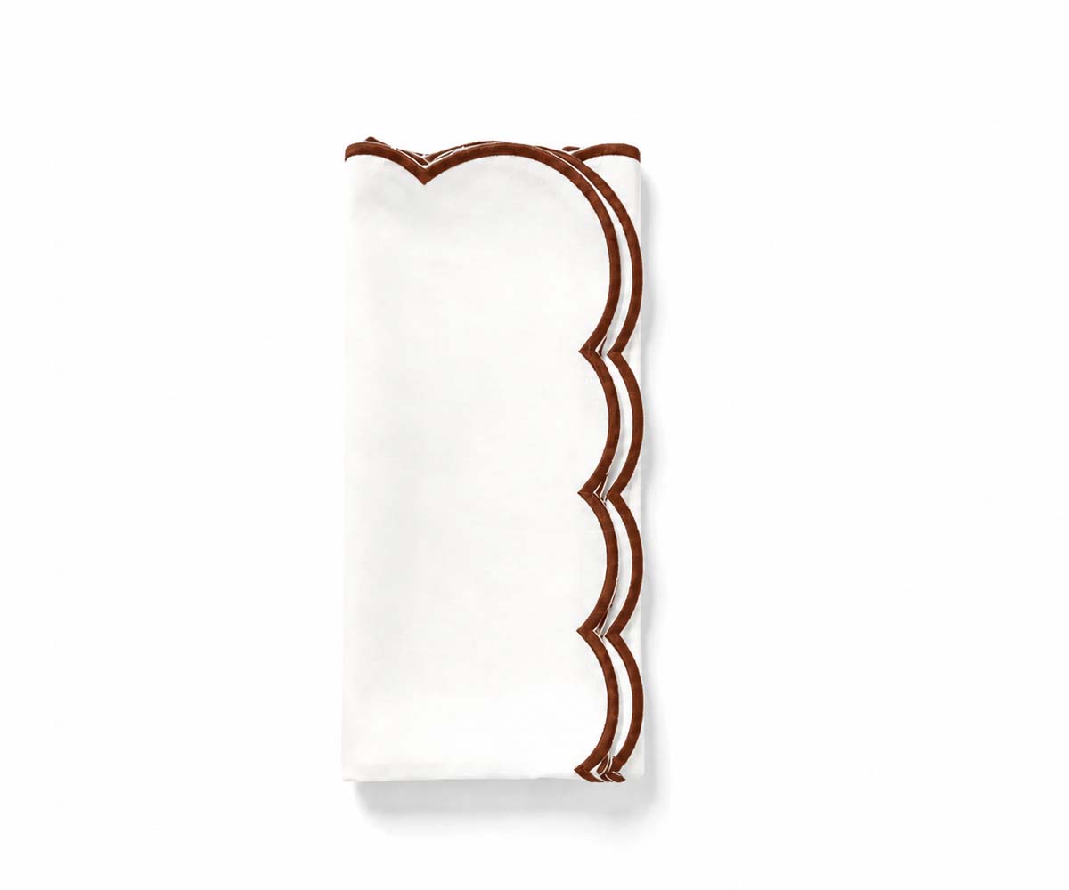 Folded white cloth napkin with a chocolate brown embroidered scalloped edge. Folded white cloth napkin with a chocolate brown embroidered scalloped edge.