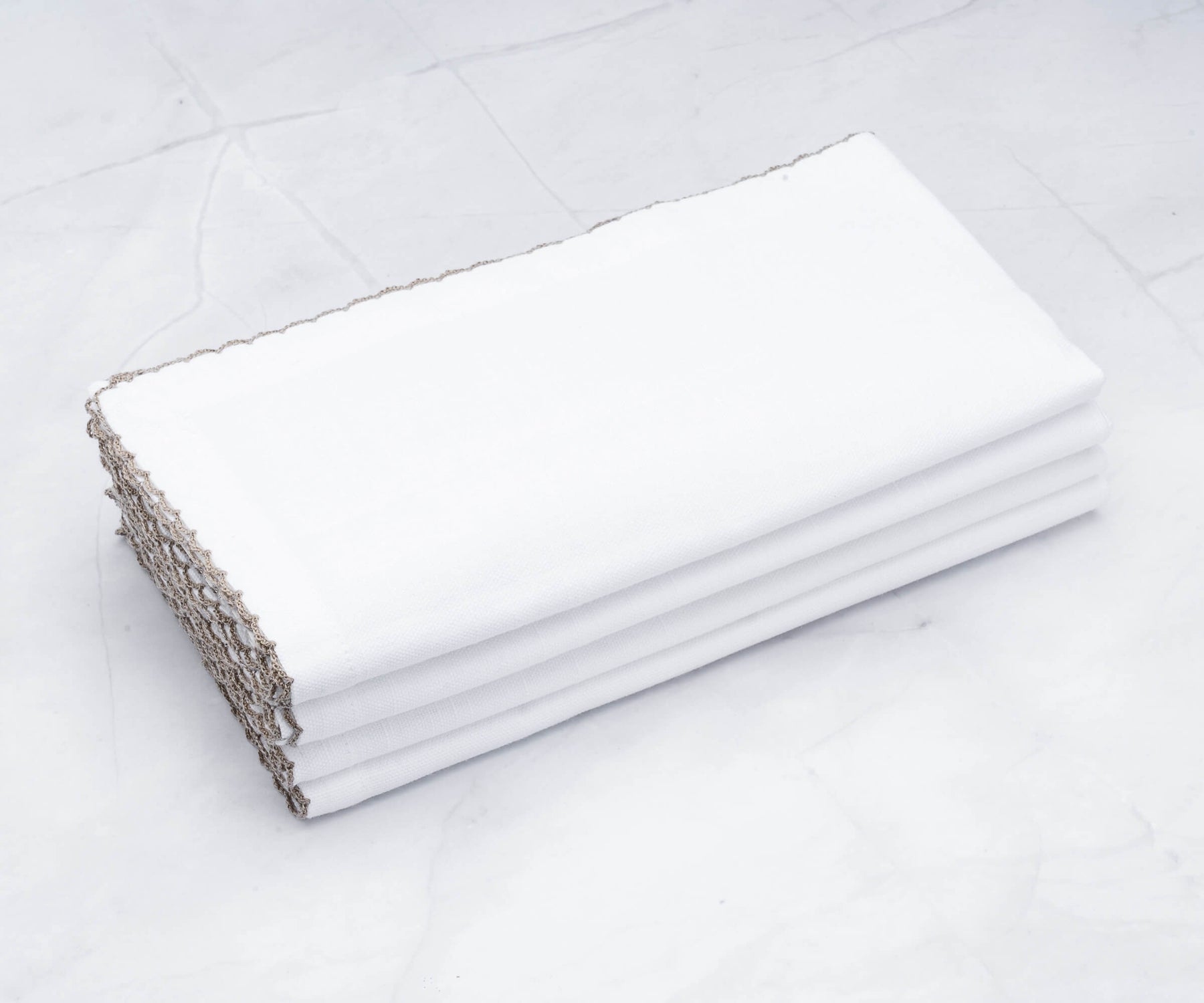 White linen wedding napkins with gold shell edging presented on a table White linen wedding napkins with gold shell edging presented on a table