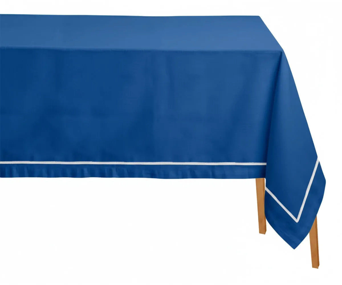 Blue rectangle cotton tablecloth with white embroidered design styled on a dining table with light blue napkins. Blue rectangle cotton tablecloth with white embroidered design styled on a dining table with light blue napkins.
