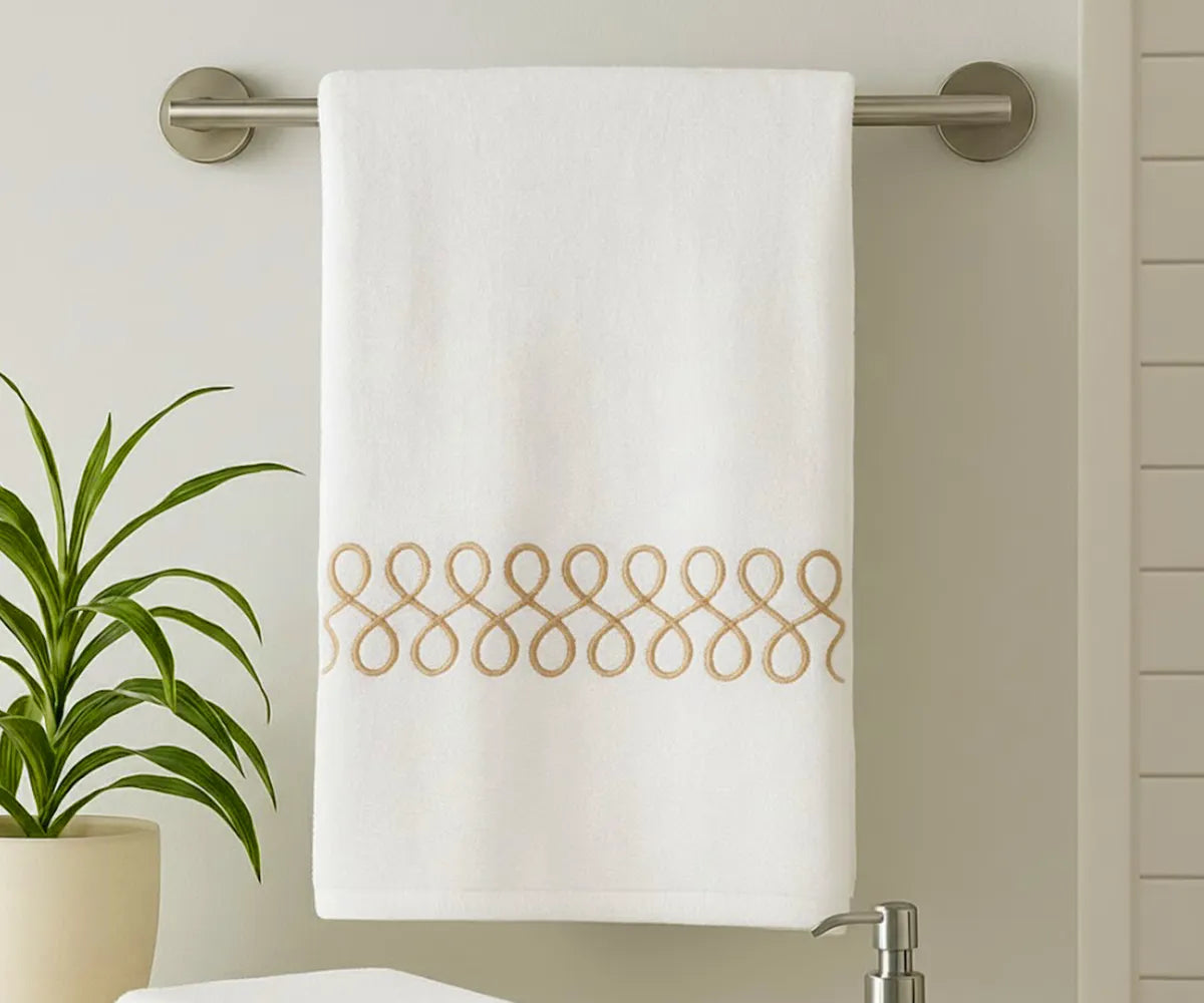 White cotton bath towel with elegant beige embroidery displayed in a modern bathroom White cotton bath towel with elegant beige embroidery displayed in a modern bathroom