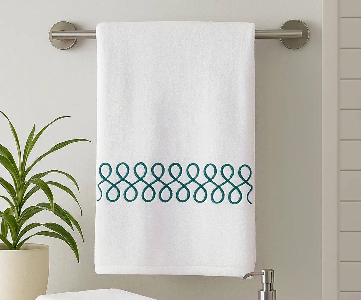 White cotton bath towel with elegant green embroidery displayed in a modern bathroom White cotton bath towel with elegant green embroidery displayed in a modern bathroom