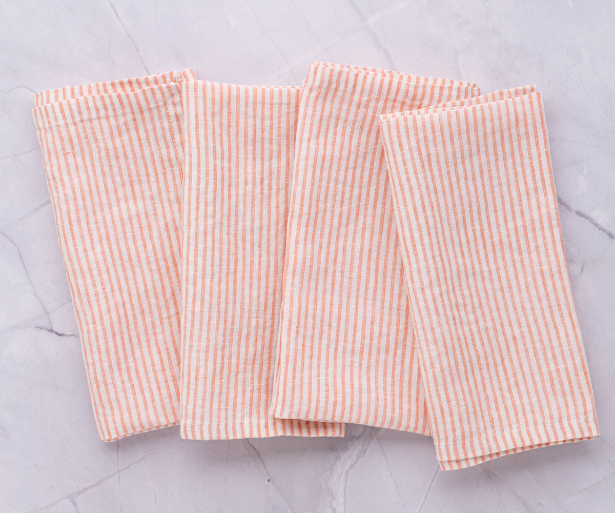 A collection of orange and white striped linen napkins arranged on a marble surface A collection of orange and white striped linen napkins arranged on a marble surface