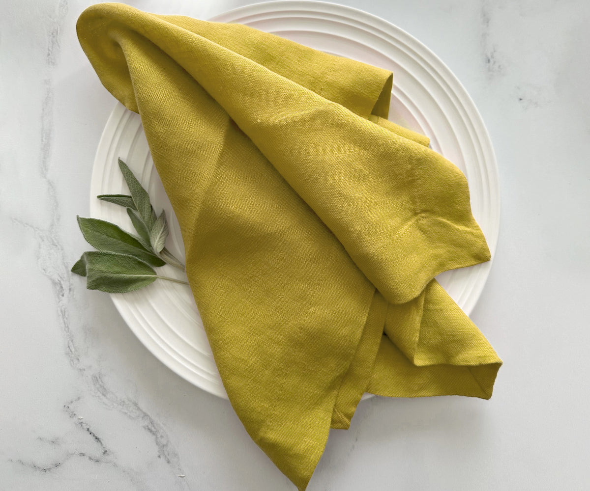 Mustard yellow linen napkin draped on a white ceramic plate with sage leaves Mustard yellow linen napkin draped on a white ceramic plate with sage leaves