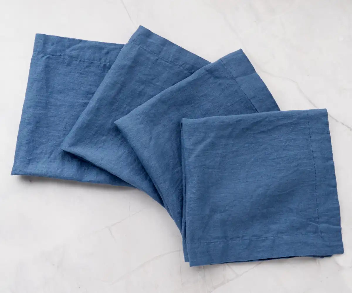 A collection of four soft blue napkins, appearing to be made of linen, neatly piled on a neutral-toned surface. A collection of four soft blue napkins, appearing to be made of linen, neatly piled on a neutral-toned surface.