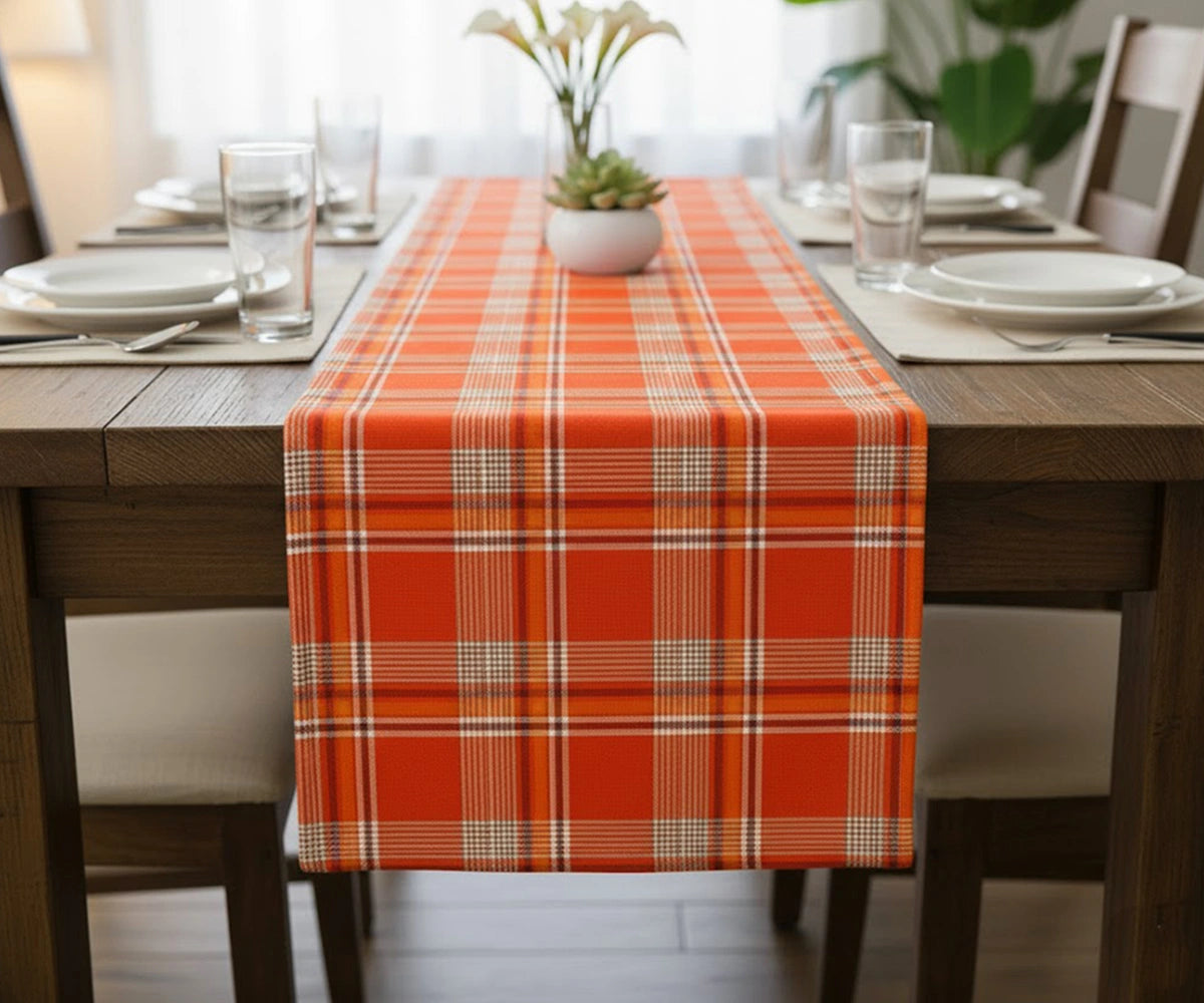 Orange-red tartan plaid cotton table runner with white, black, and yellow checks adding a vibrant festive touch to a Christmas dining table. Orange-red tartan plaid cotton table runner with white, black, and yellow checks adding a vibrant festive touch to a Christmas dining table.