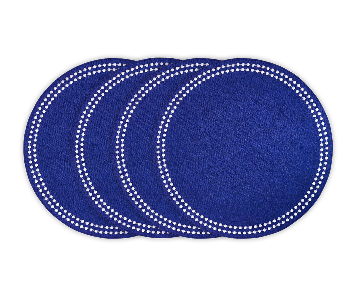 Blue cotton round placemat with white embroidered dot trim on a dining table Blue cotton round placemat with white embroidered dot trim on a dining table