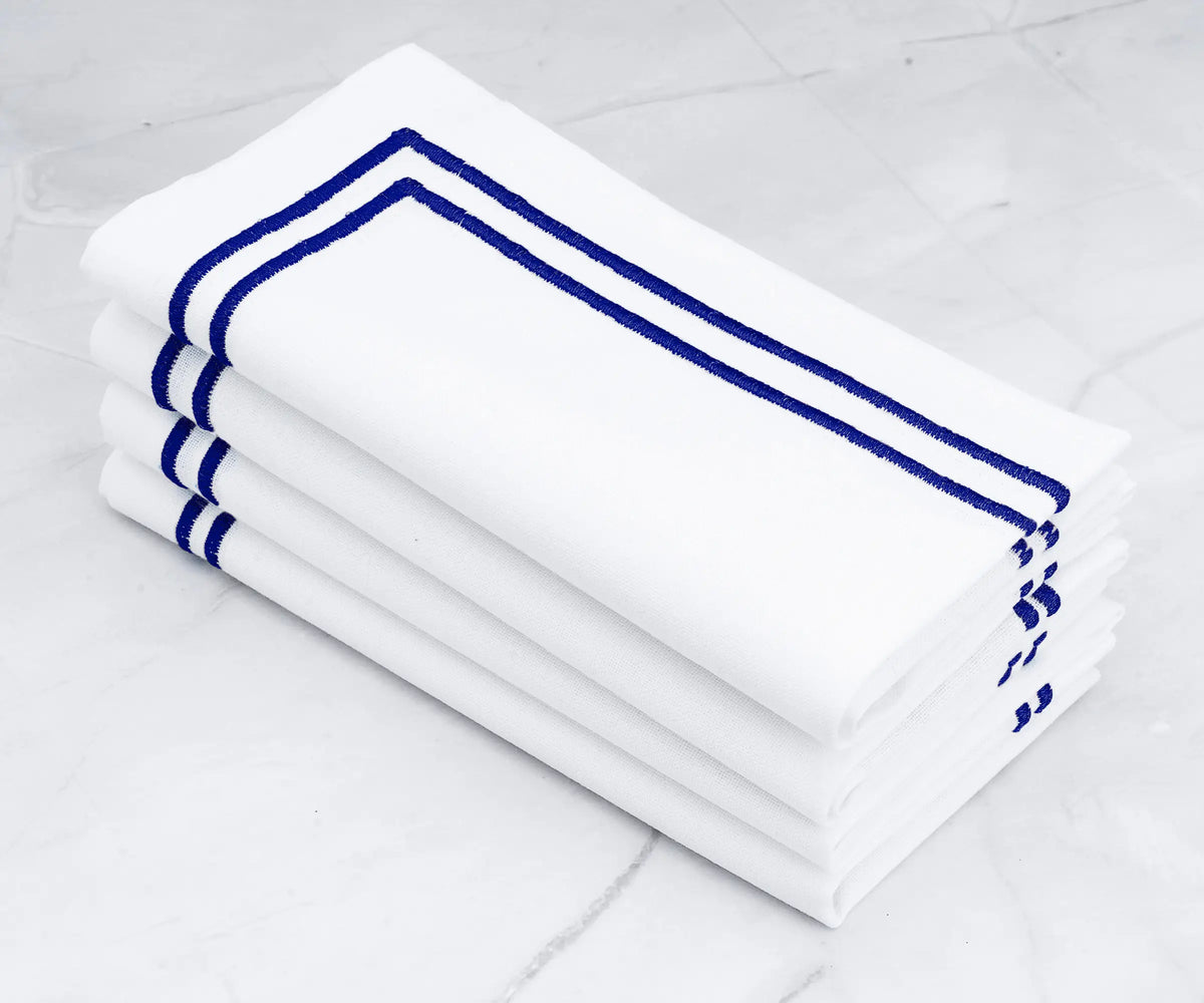 Fine linen napkins adorned with a double line of royal blue embroidery. Fine linen napkins adorned with a double line of royal blue embroidery.
