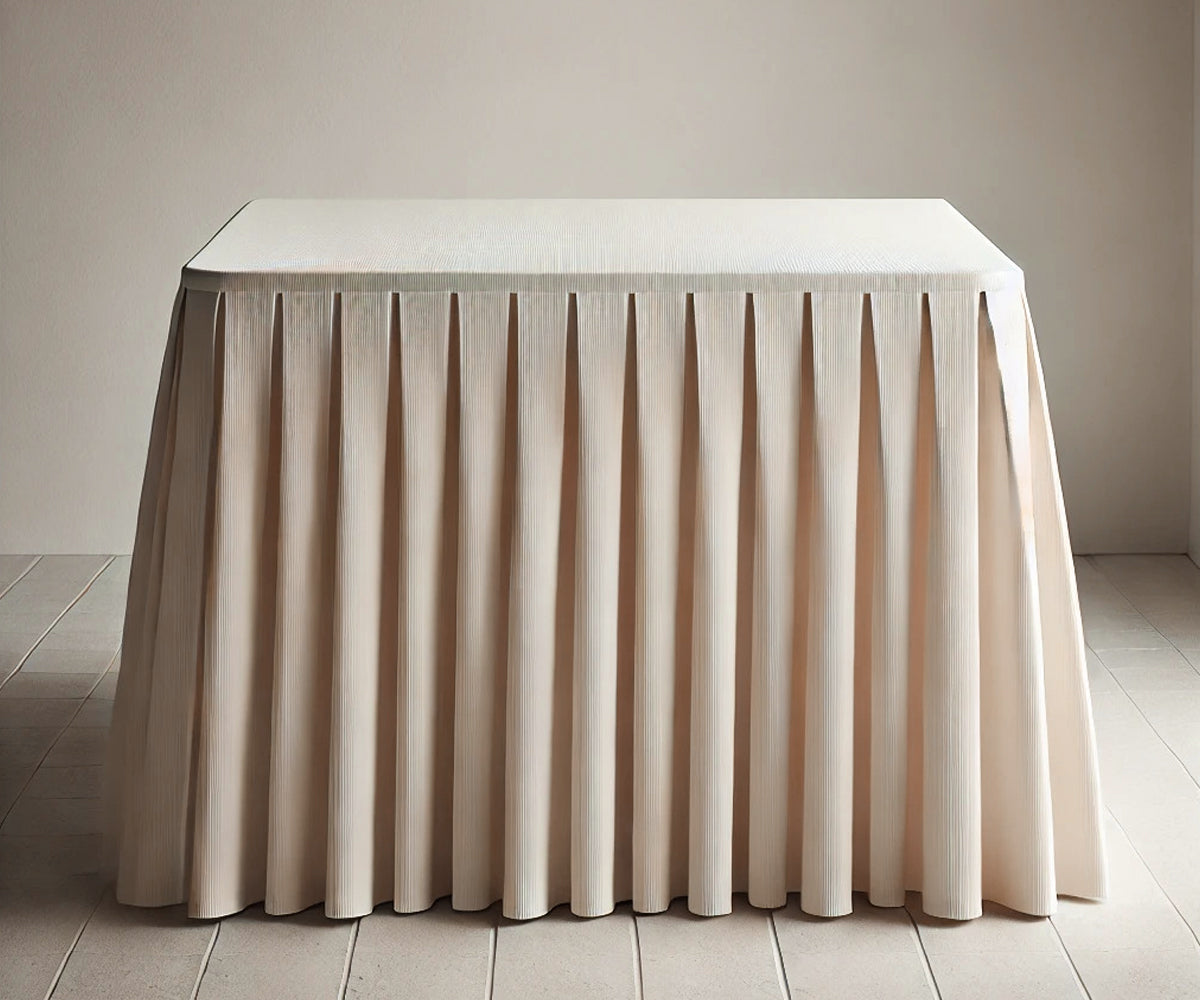 Fabric table skirt in soft beige cotton covering a party table with decorative pleats Fabric table skirt in soft beige cotton covering a party table with decorative pleats