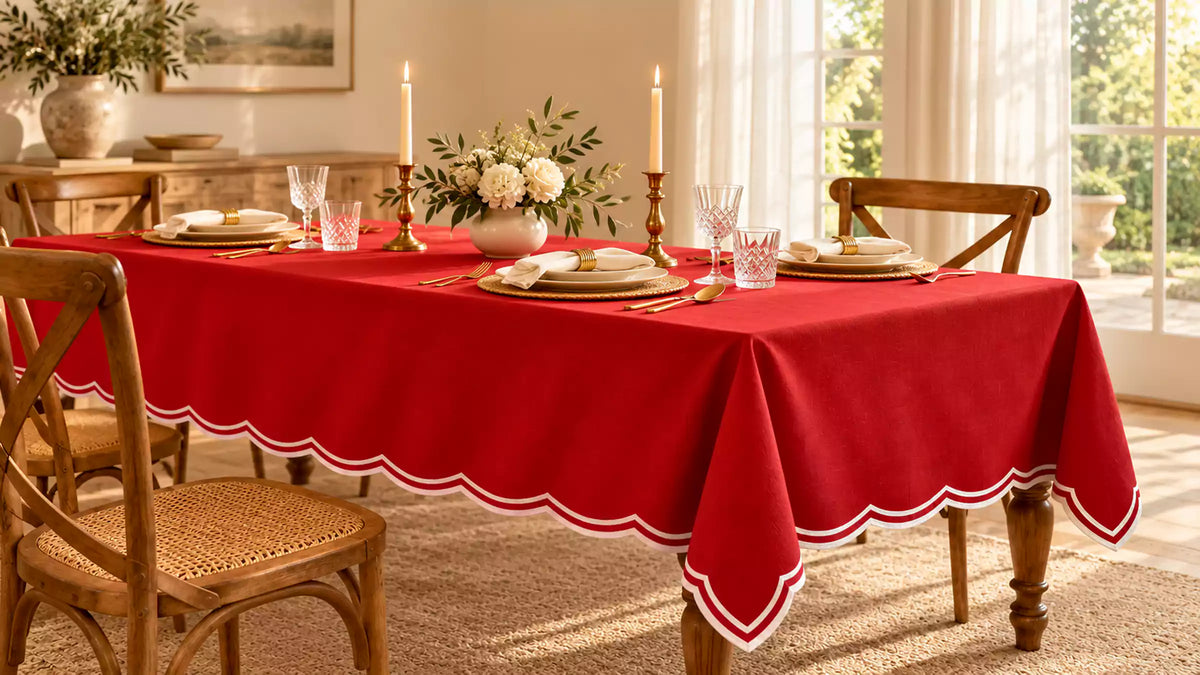 Red tablecloth with a white-trimmed scalloped edge on a dining table set with candles and white napkins.