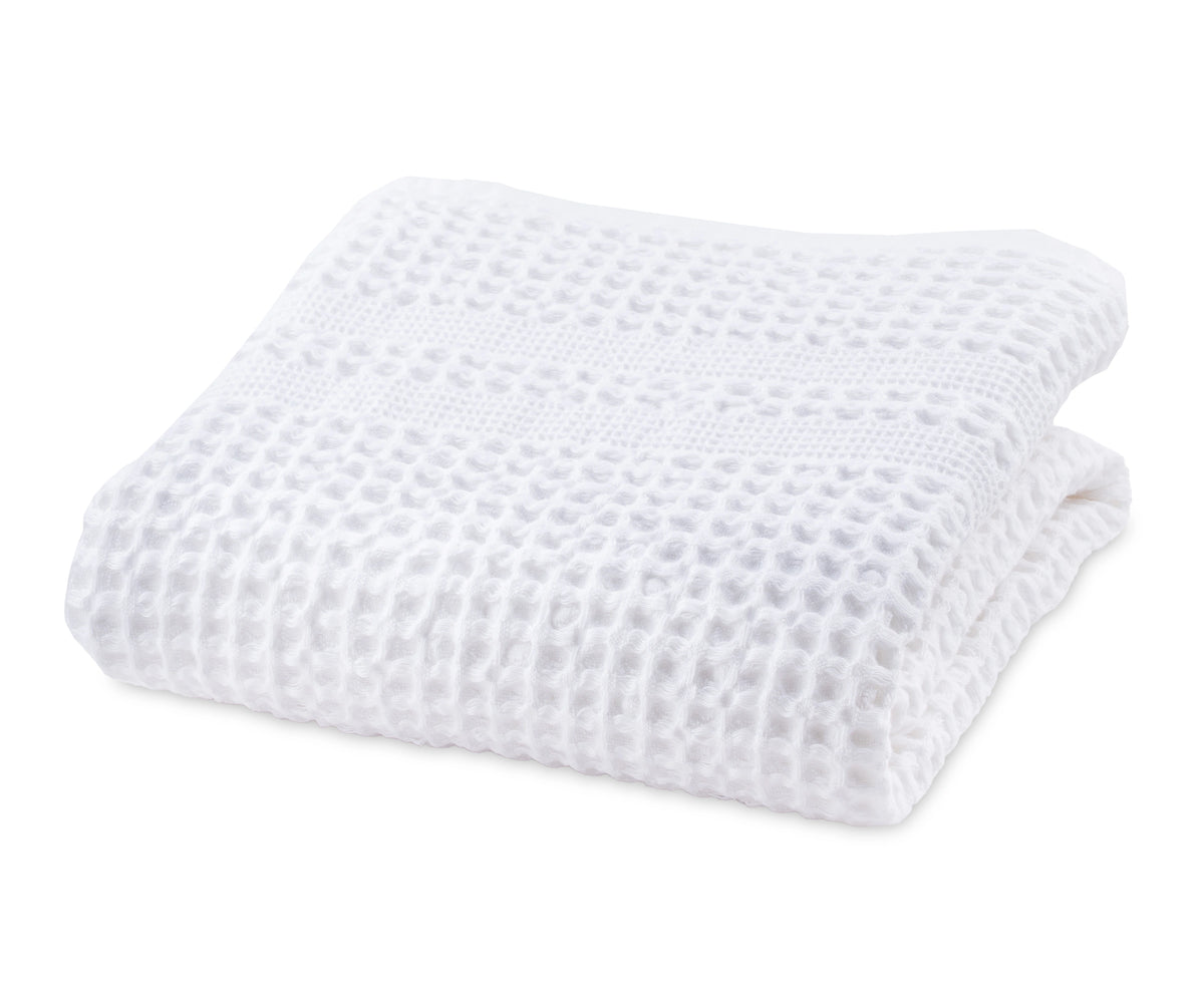 White cotton waffle blanket neatly folded on a bed for a cozy look. White cotton waffle blanket neatly folded on a bed for a cozy look.