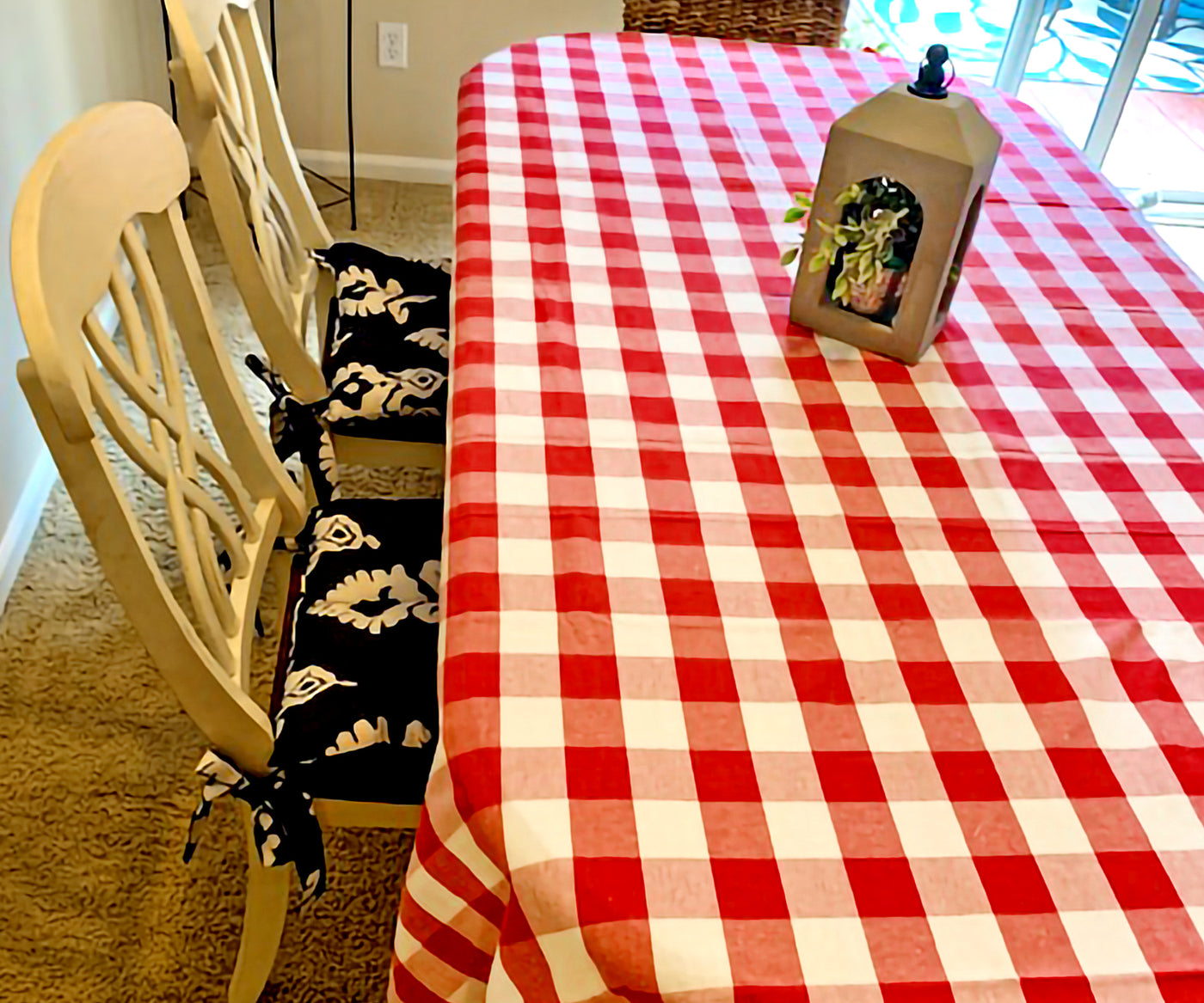 Dining table with a red and white checkered tablecloth, wooden chairs with patterned cushions, and a decorative lantern Dining table with a red and white checkered tablecloth, wooden chairs with patterned cushions, and a decorative lantern