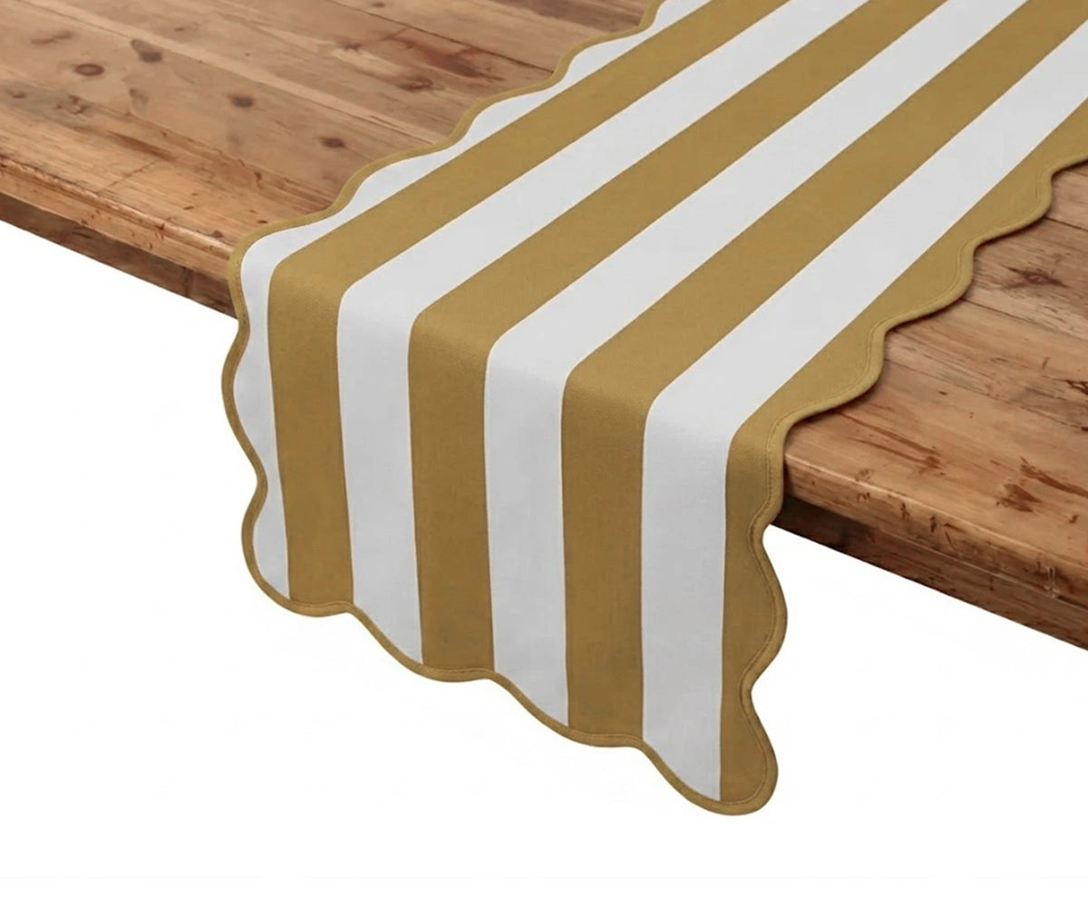 Mustard yellow and white cabana striped table runner with scalloped edges laid across a wooden table. Mustard yellow and white cabana striped table runner with scalloped edges laid across a wooden table.