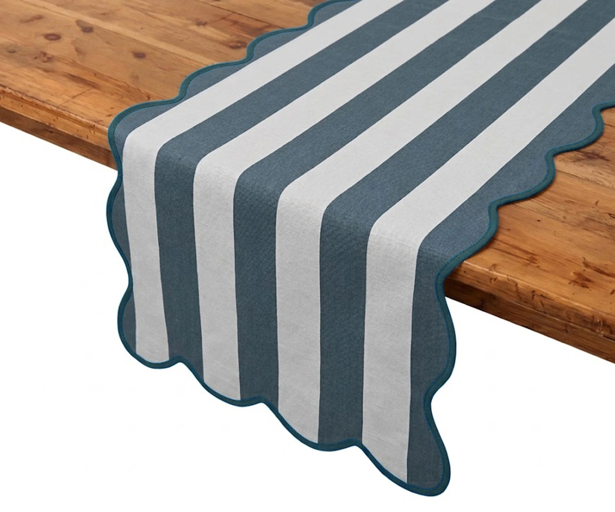 Ocean blue and white cabana striped table runner with scalloped edges hanging over a rustic wooden table. Ocean blue and white cabana striped table runner with scalloped edges hanging over a rustic wooden table.