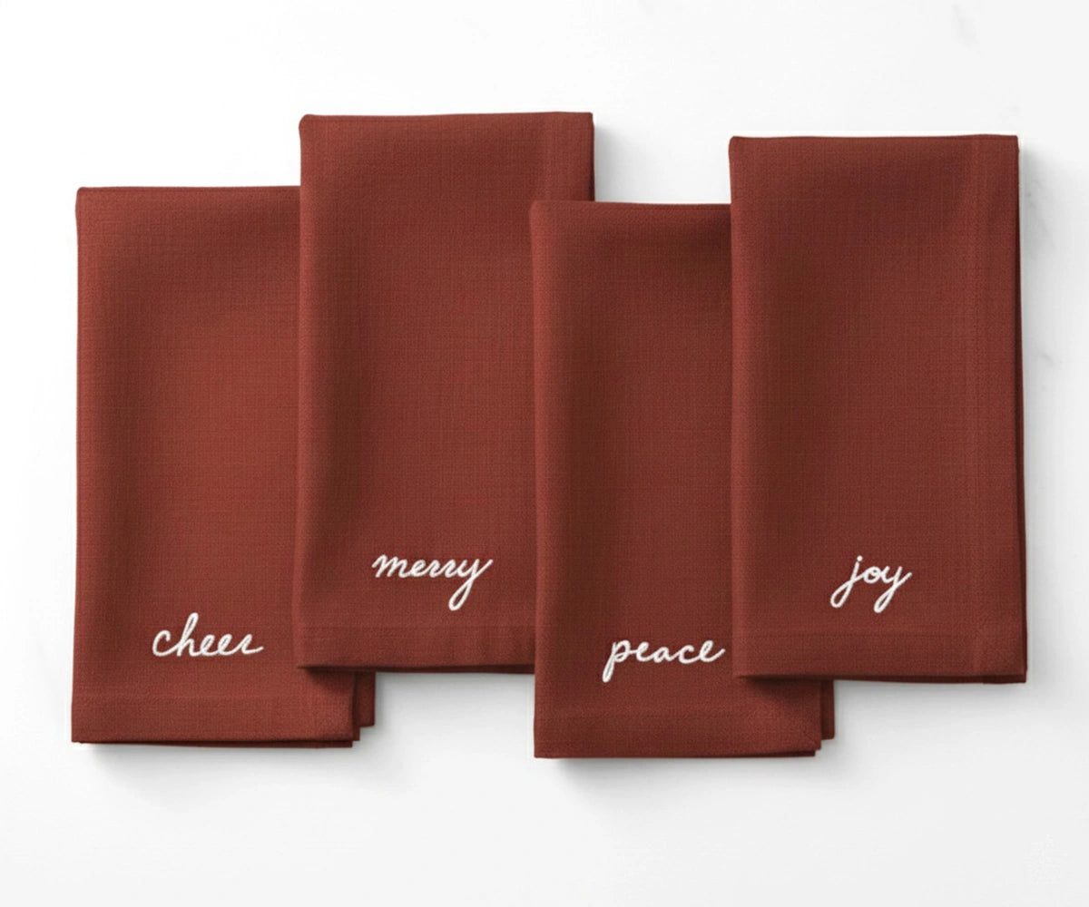 Deep red holiday napkin featuring white stitched Christmas sentiments for an elegant seasonal table. Deep red holiday napkin featuring white stitched Christmas sentiments for an elegant seasonal table.