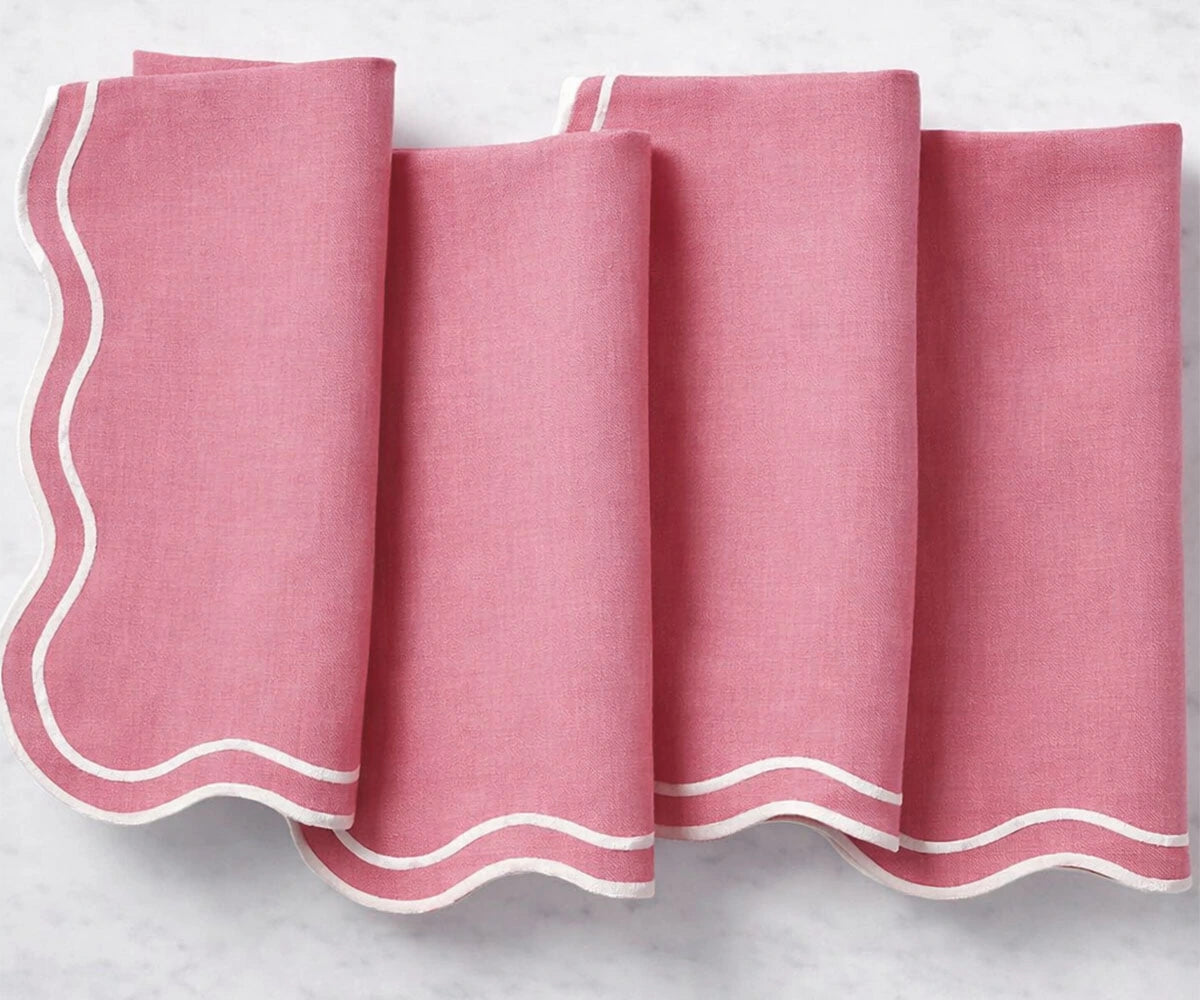 A set of pink cloth napkins with scalloped embroidered borders, neatly folded and displayed. A set of pink cloth napkins with scalloped embroidered borders, neatly folded and displayed.