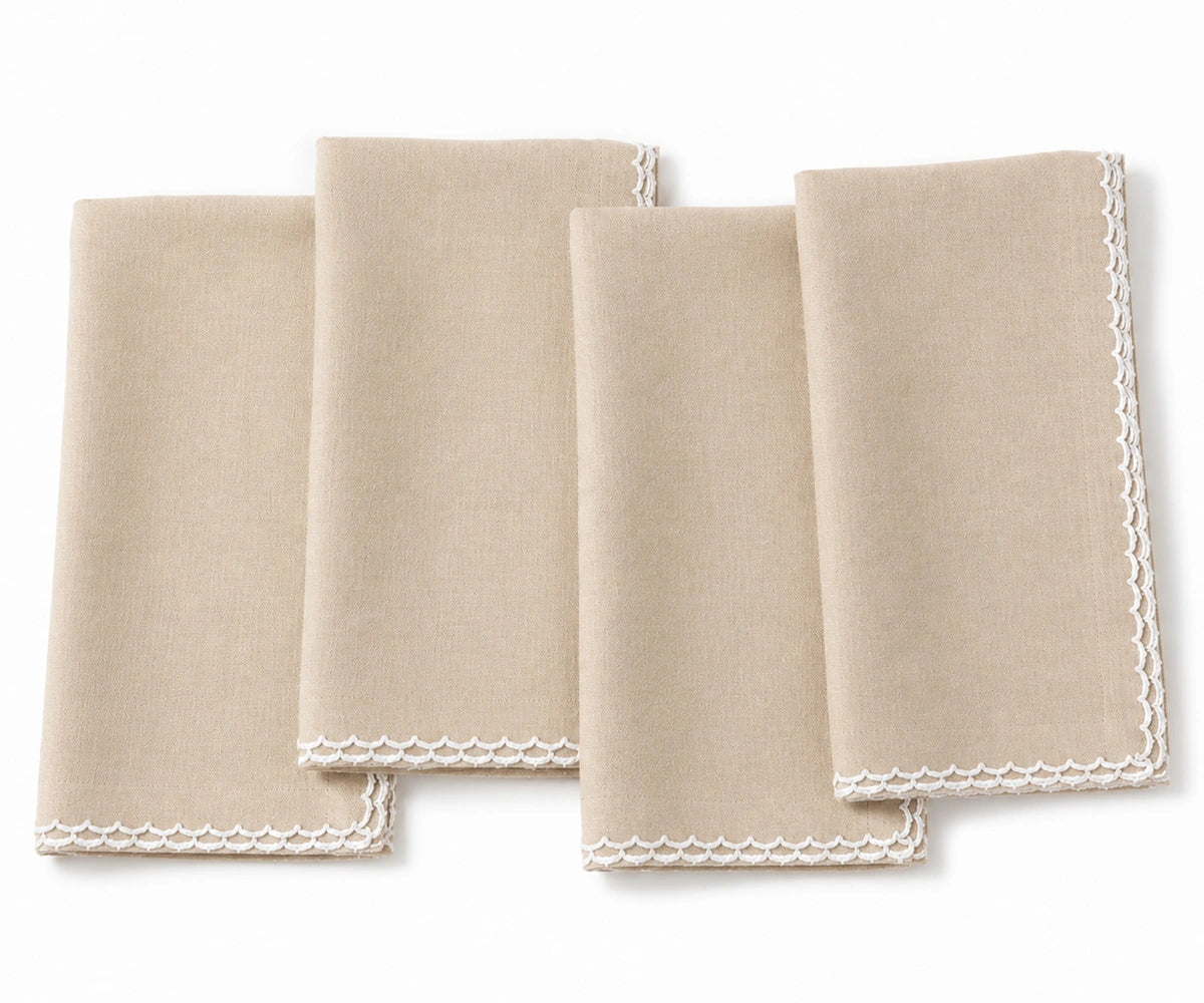 Four folded beige cloth napkins with white scalloped edges, arranged overlapping on a white background. Four folded beige cloth napkins with white scalloped edges, arranged overlapping on a white background.