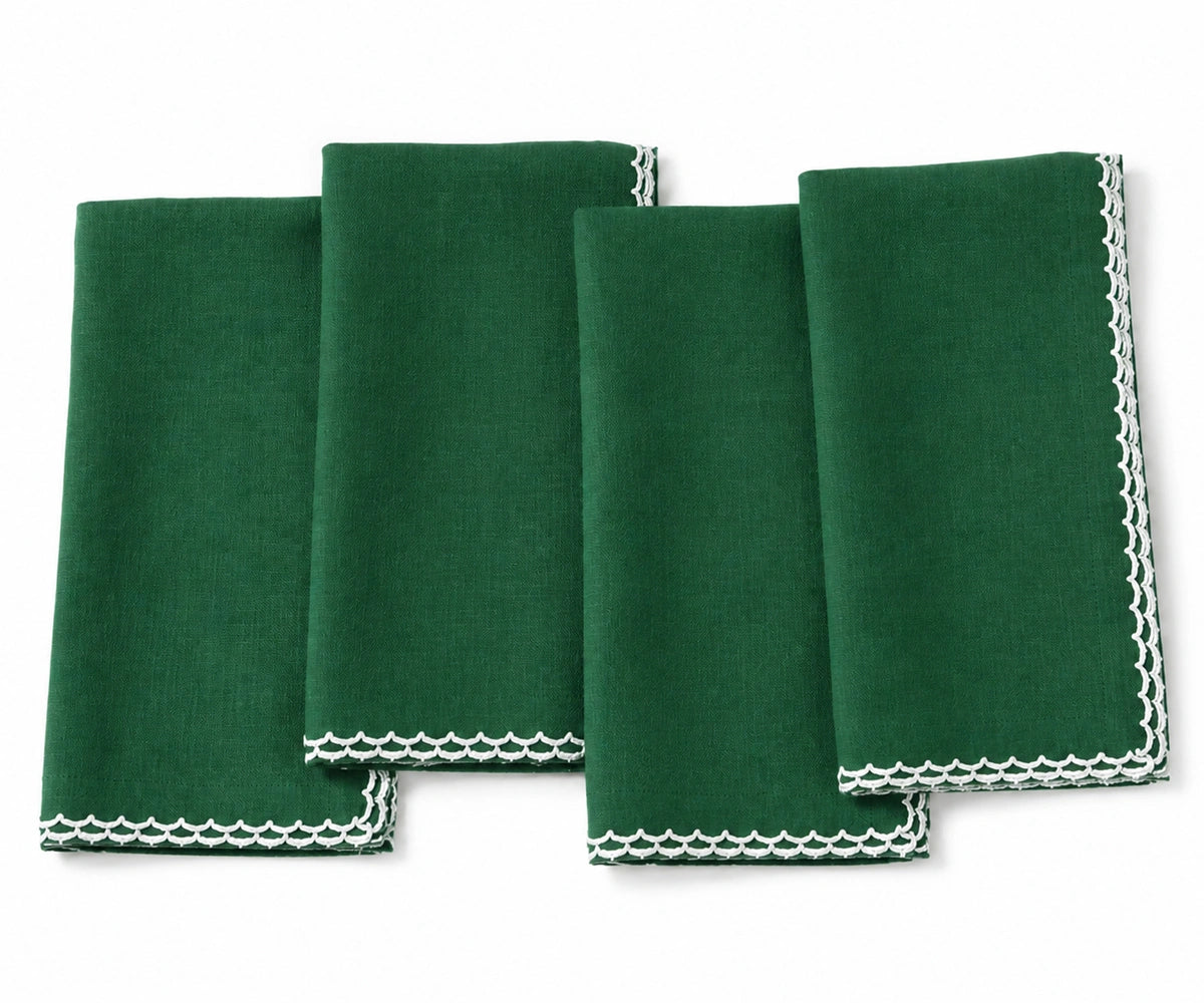 Four green folded cloth napkins with white scalloped edges, arranged overlapping on a plain white background. Four green folded cloth napkins with white scalloped edges, arranged overlapping on a plain white background.