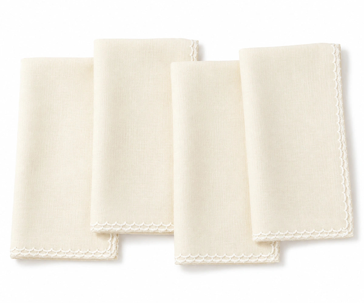 Four ivory colored cotton napkins with delicate embroidered borders, arranged overlapping on a white background. Four ivory colored cotton napkins with delicate embroidered borders, arranged overlapping on a white background.