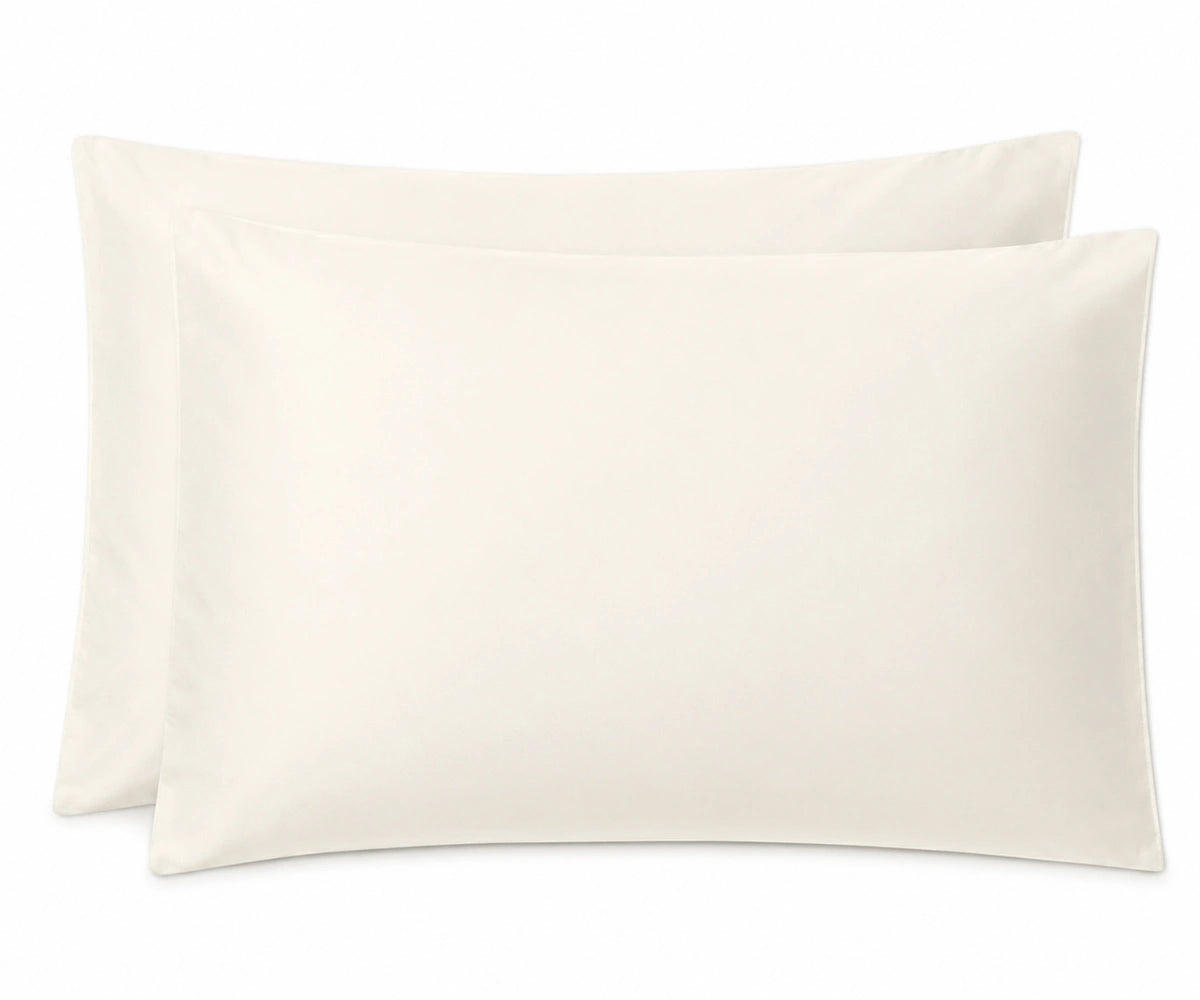 Two plain ivory pillowcases stacked slightly offset against a clean white background. Two plain ivory pillowcases stacked slightly offset against a clean white background.