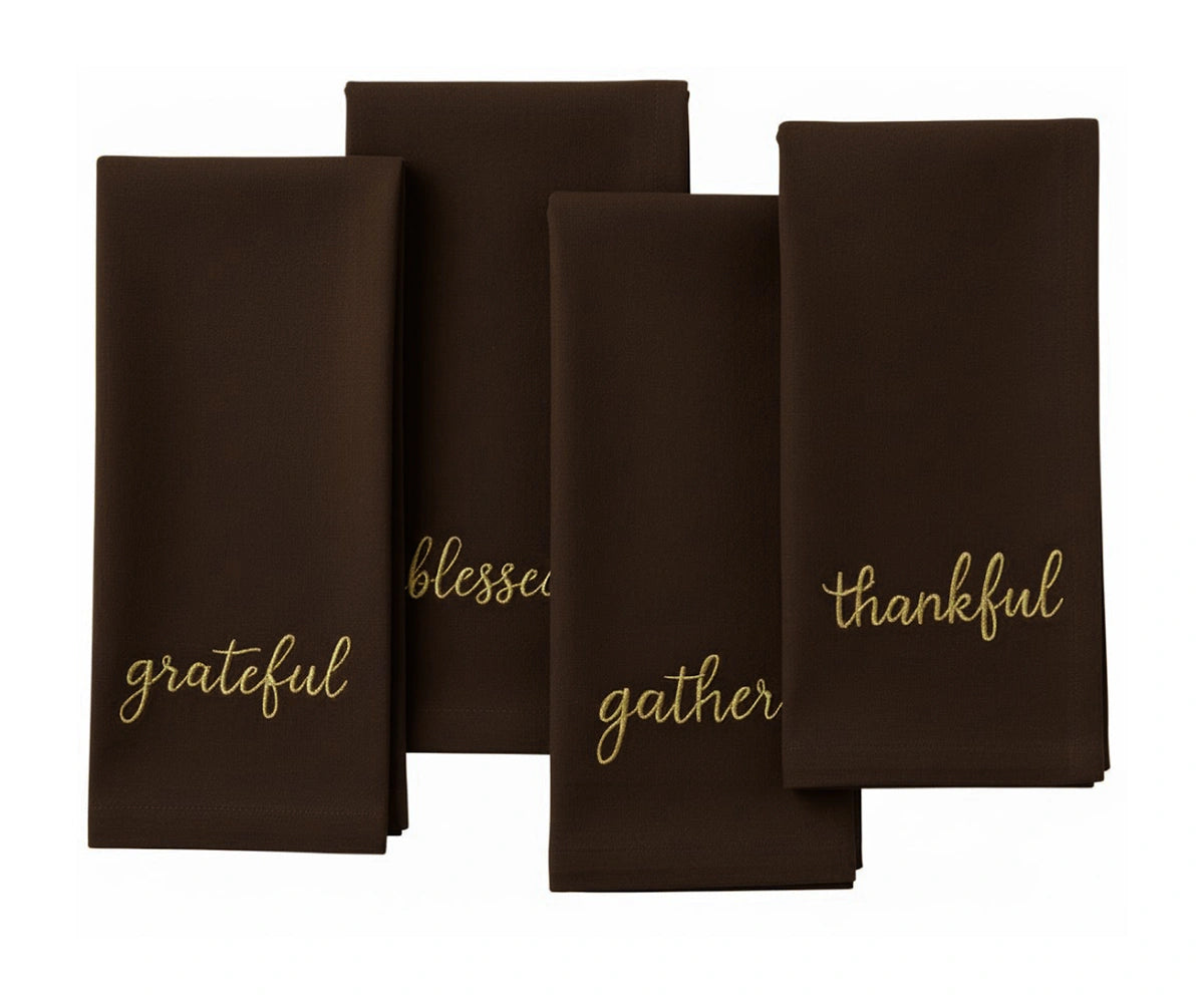 Brown holiday napkin featuring gold stitched words – Grateful, Blessed, Gather, Thankful. Brown holiday napkin featuring gold stitched words – Grateful, Blessed, Gather, Thankful.