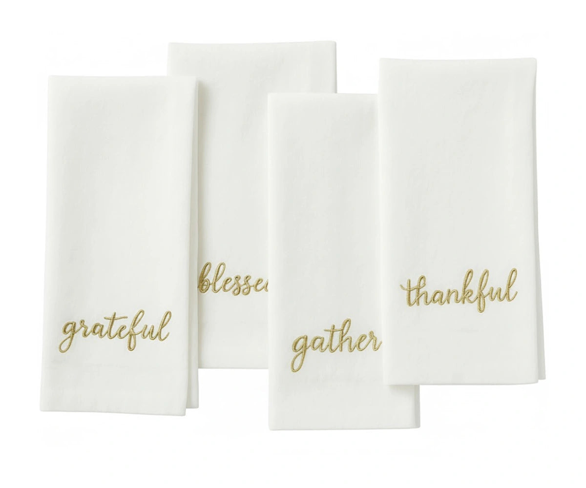 White sentiment embroidered table napkin with gold stitched holiday phrases for Christmas dining. White sentiment embroidered table napkin with gold stitched holiday phrases for Christmas dining.