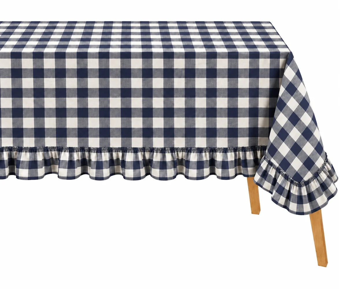 A navy blue and white gingham checkered tablecloth with a ruffled hem, draped over a table with light wood legs against a plain white background. A navy blue and white gingham checkered tablecloth with a ruffled hem, draped over a table with light wood legs against a plain white background.