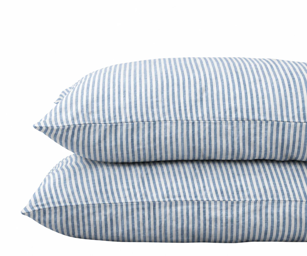 Pair of stacked pillows in dusty blue and white striped linen pillowcases against a plain white background. Pair of stacked pillows in dusty blue and white striped linen pillowcases against a plain white background.