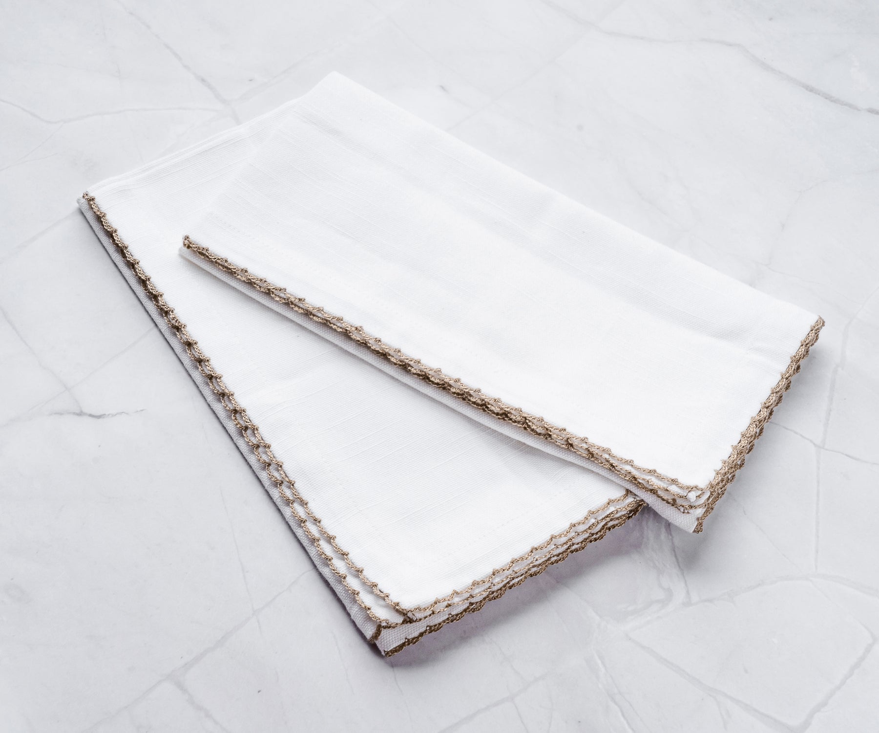 White napkins with beige edge bunting stitch, folded on marble. White napkins with beige edge bunting stitch, folded on marble.