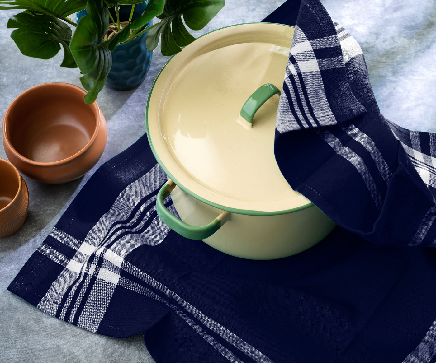 Cream pot with a green handle, placed on a navy blue plaid kitchen towel, with bowls. Cream pot with a green handle, placed on a navy blue plaid kitchen towel, with bowls.