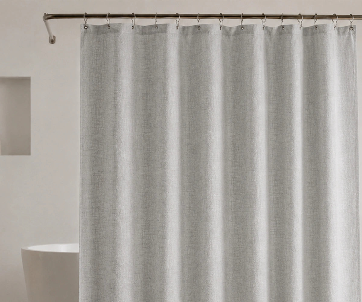 A light gray textured shower curtain hanging from a dark metal rod with silver rings, shown in a minimalist bathroom setting with a white bathtub edge visible on the left. A light gray textured shower curtain hanging from a dark metal rod with silver rings, shown in a minimalist bathroom setting with a white bathtub edge visible on the left.