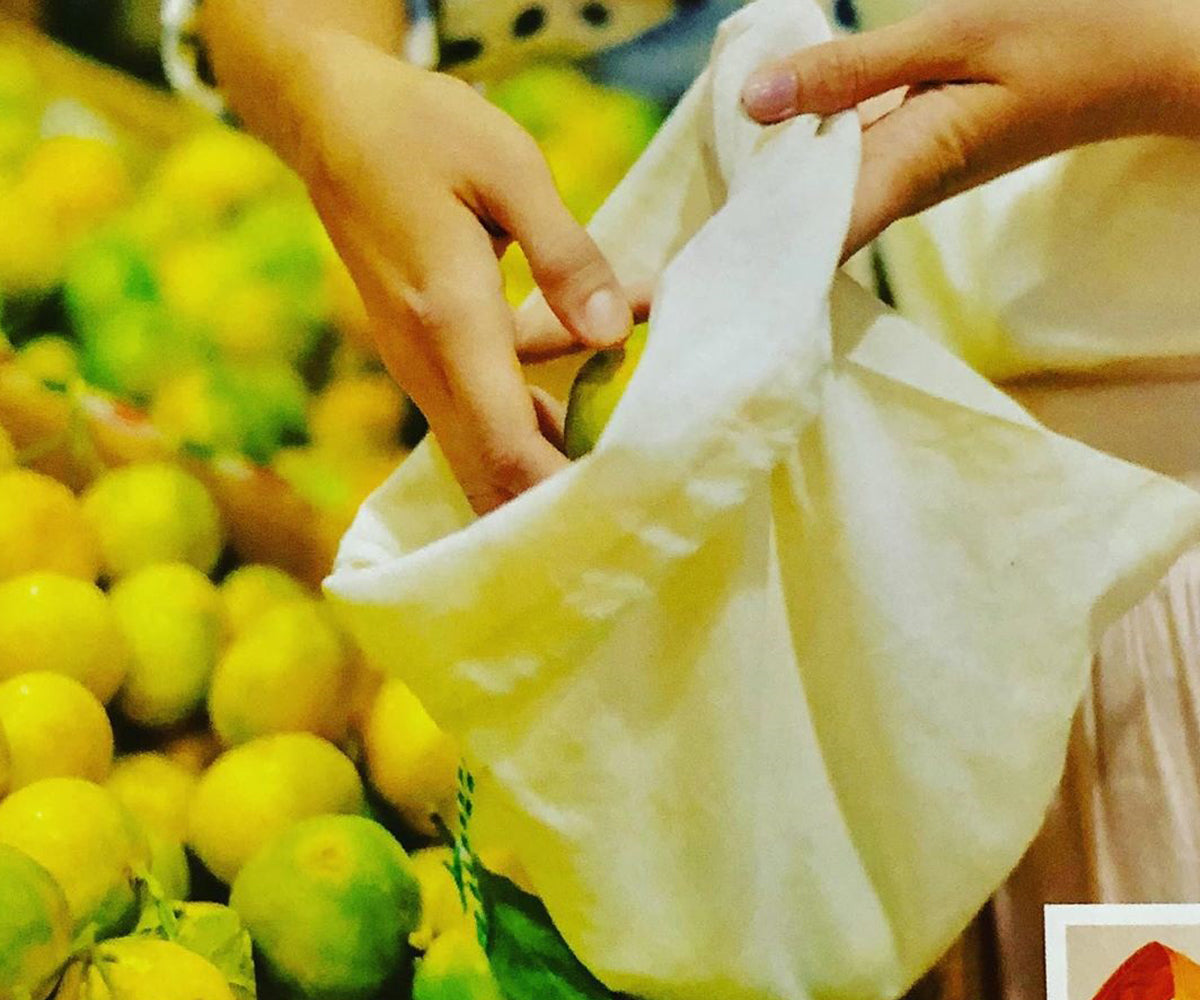 Hands placing a lemon into a reusable muslin bag at a fruit market. Hands placing a lemon into a reusable muslin bag at a fruit market.