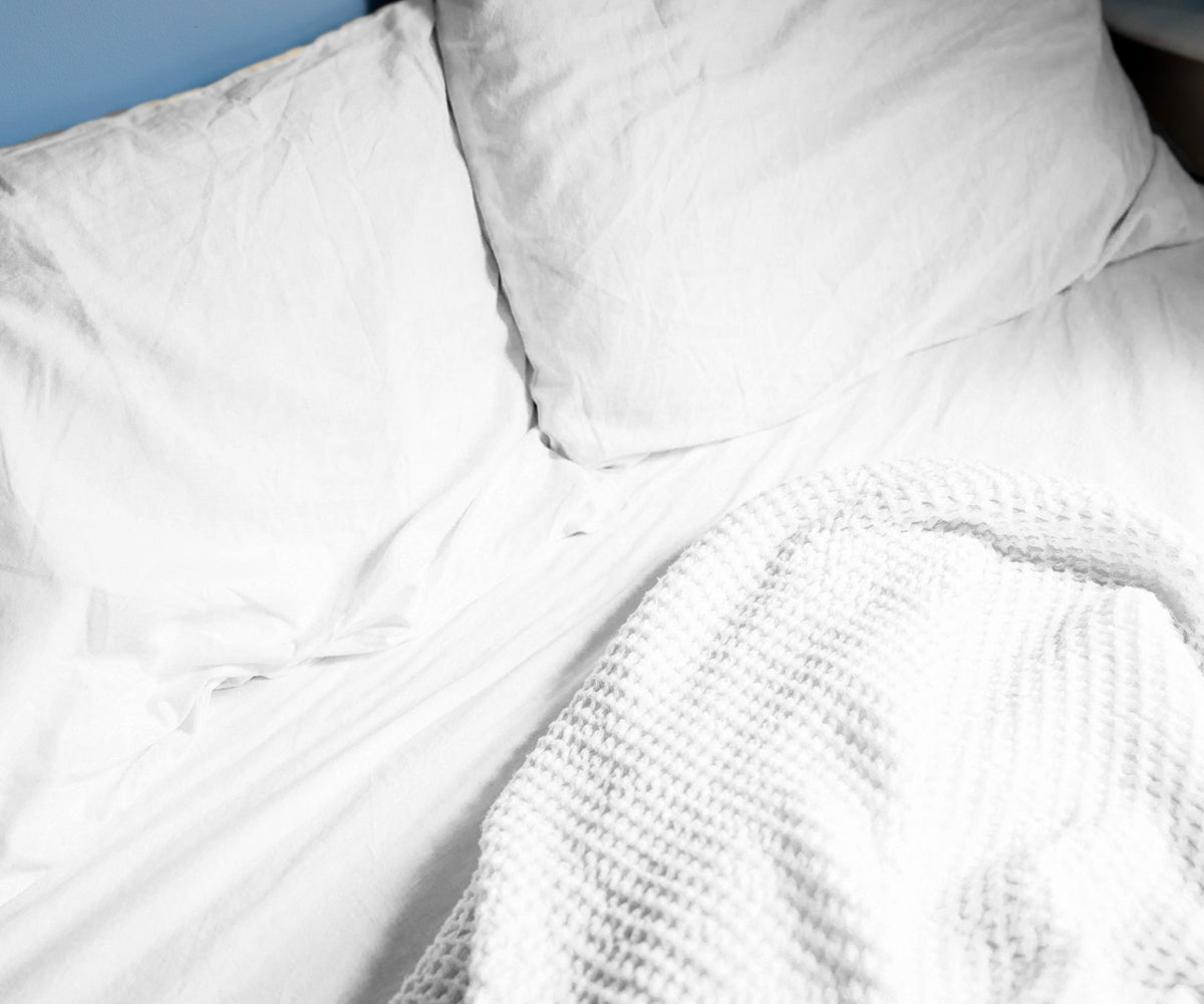 Bed dressed with white cotton fitted sheet, blanket, and pillows