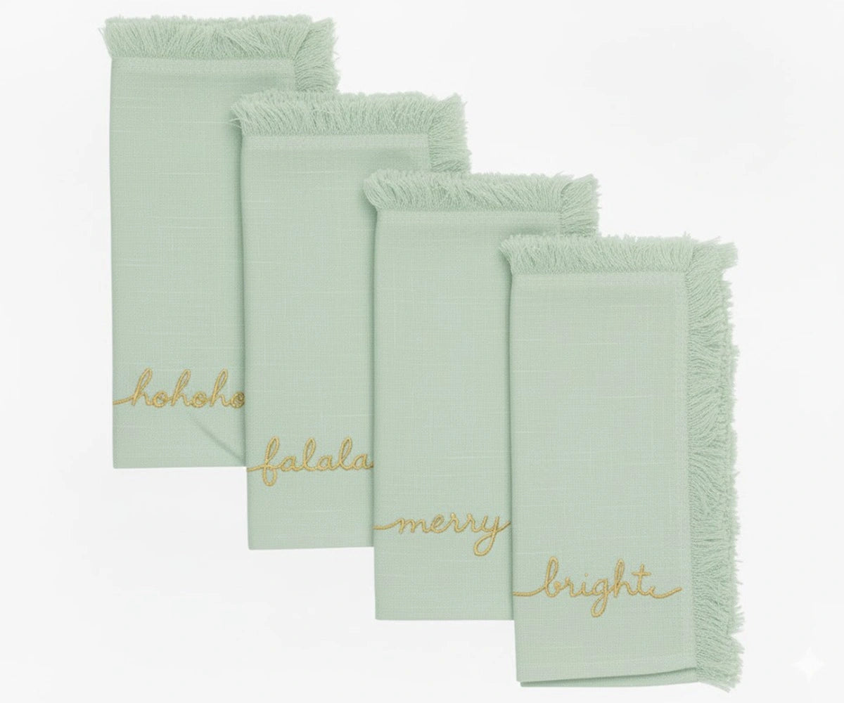 Sage green embroidered holiday napkins with gold stitched words and fringed edges for festive dining and Christmas celebrations Sage green embroidered holiday napkins with gold stitched words and fringed edges for festive dining and Christmas celebrations