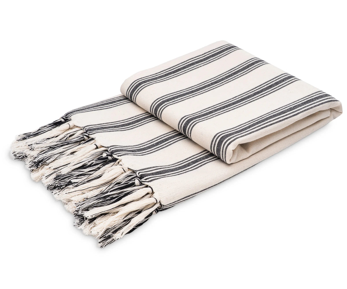 Black and white striped cotton throw blanket with tassel fringe styled on a sofa Black and white striped cotton throw blanket with tassel fringe styled on a sofa