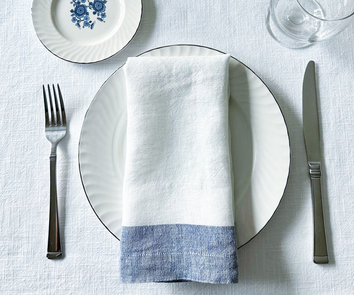 Premium white linen napkins neatly stacked ready for a dinner setting. These high-quality dinner napkins, available in a variety of shades such as blue and white, black and white, and white and gold, offer a luxurious touch to any meal. 