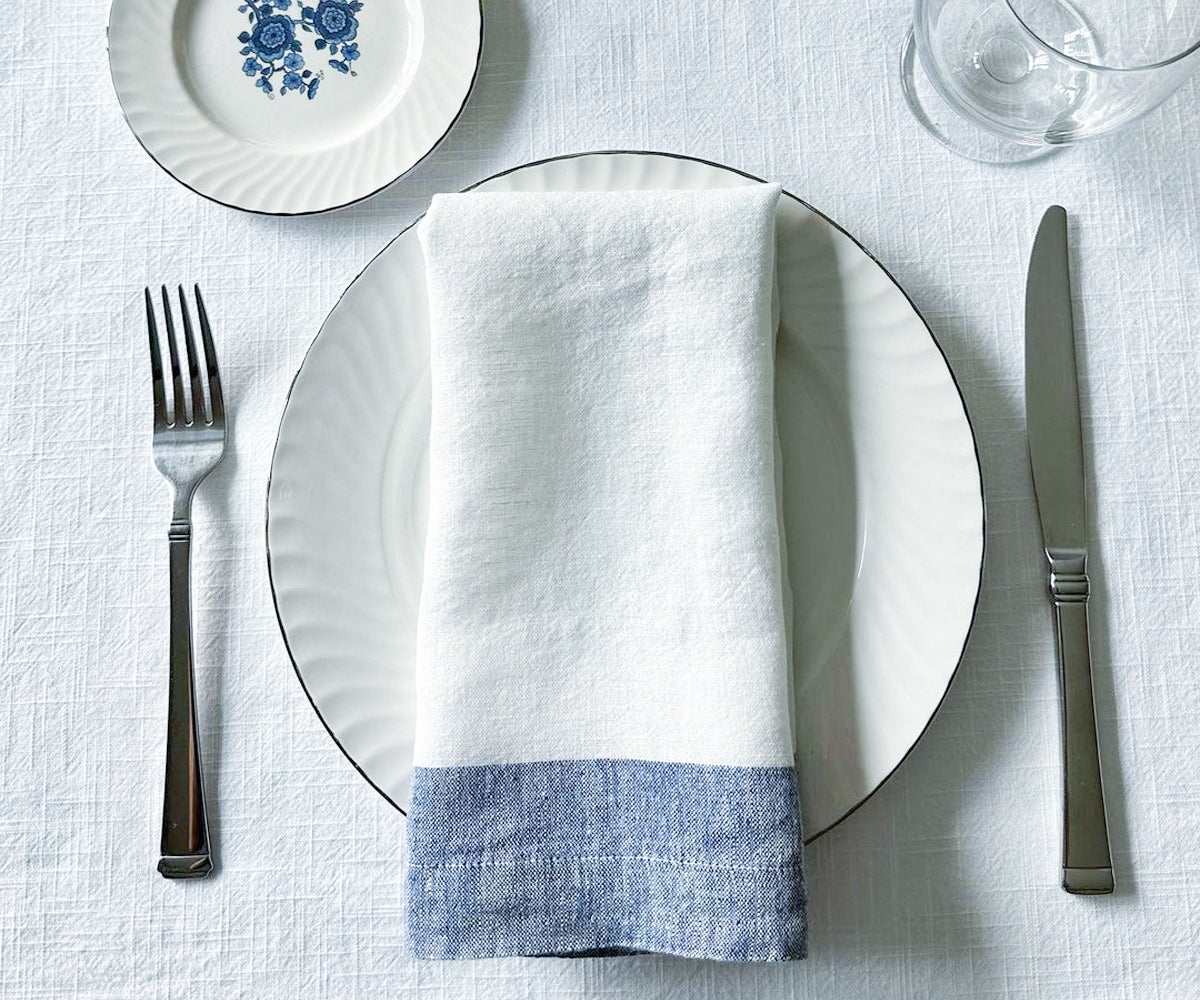 Premium white linen napkins neatly stacked ready for a dinner setting. These high-quality dinner napkins, available in a variety of shades such as blue and white, black and white, and white and gold, offer a luxurious touch to any meal.  Premium white linen napkins neatly stacked ready for a dinner setting. These high-quality dinner napkins, available in a variety of shades such as blue and white, black and white, and white and gold, offer a luxurious touch to any meal.