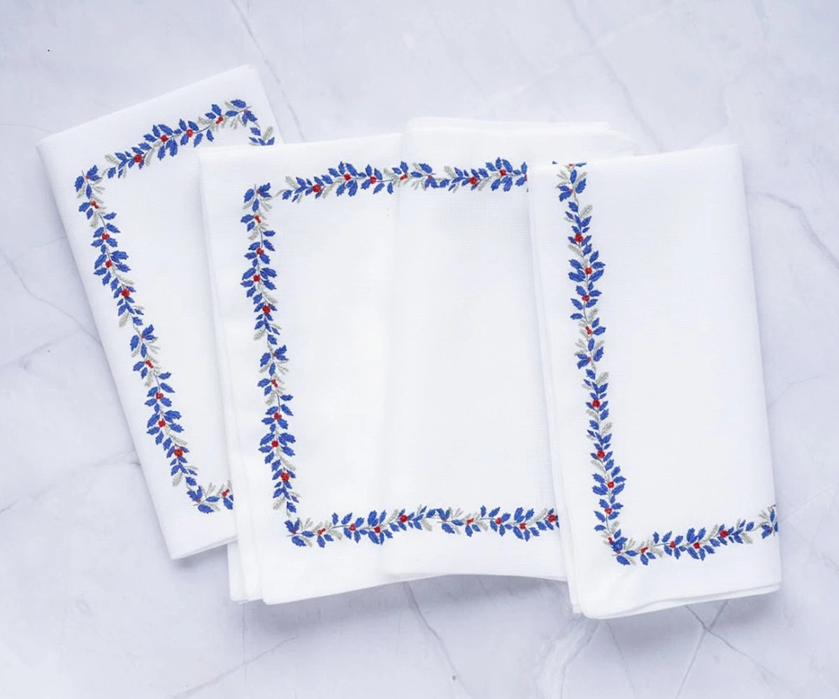 Set of white cotton napkins with a refined stitched leaf border design in blue, red, and soft grey, adding a classic touch to any table setting. Set of white cotton napkins with a refined stitched leaf border design in blue, red, and soft grey, adding a classic touch to any table setting.
