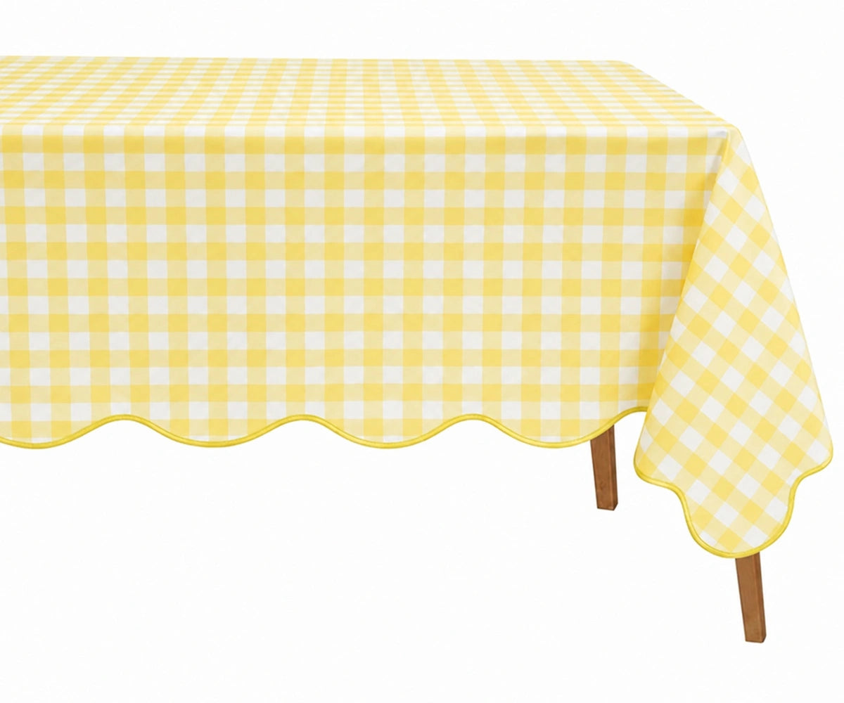 Yellow and white checkered cotton tablecloth with a decorative scalloped edge draped over a table. Yellow and white checkered cotton tablecloth with a decorative scalloped edge draped over a table.