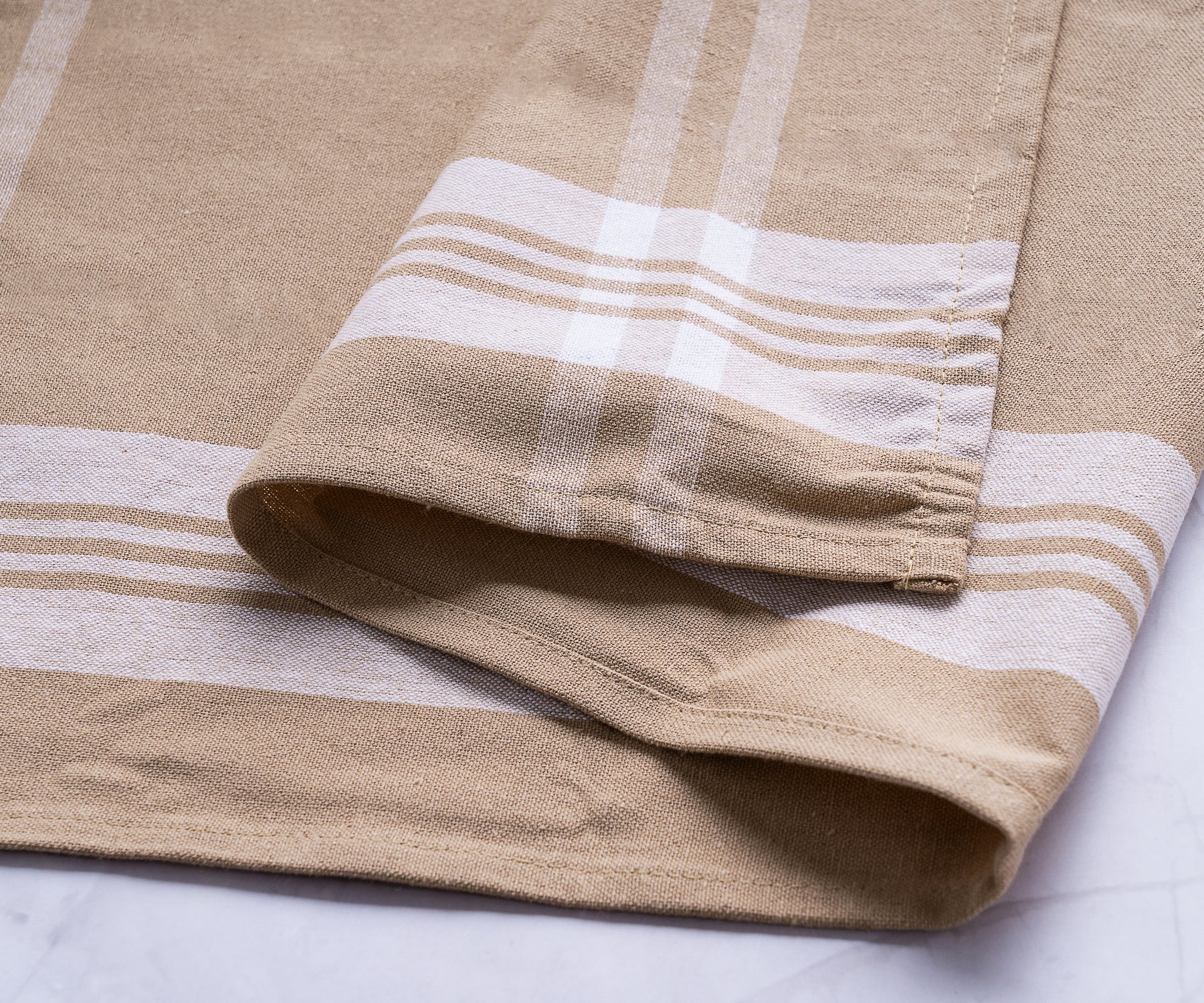 Detailed view of a beige farmhouse kitchen towel with white and tan stripes Detailed view of a beige farmhouse kitchen towel with white and tan stripes