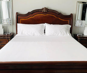 Bed with white cotton fitted sheets and a wooden headboard