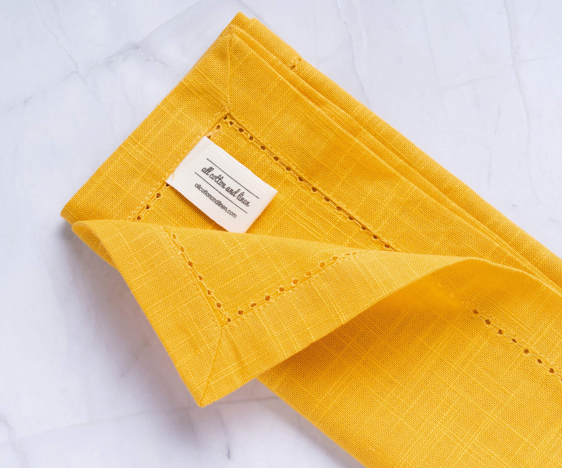 A folded yellow cloth dinner napkins with the label of All cotton and linen. A folded yellow cloth dinner napkins with the label of All cotton and linen.